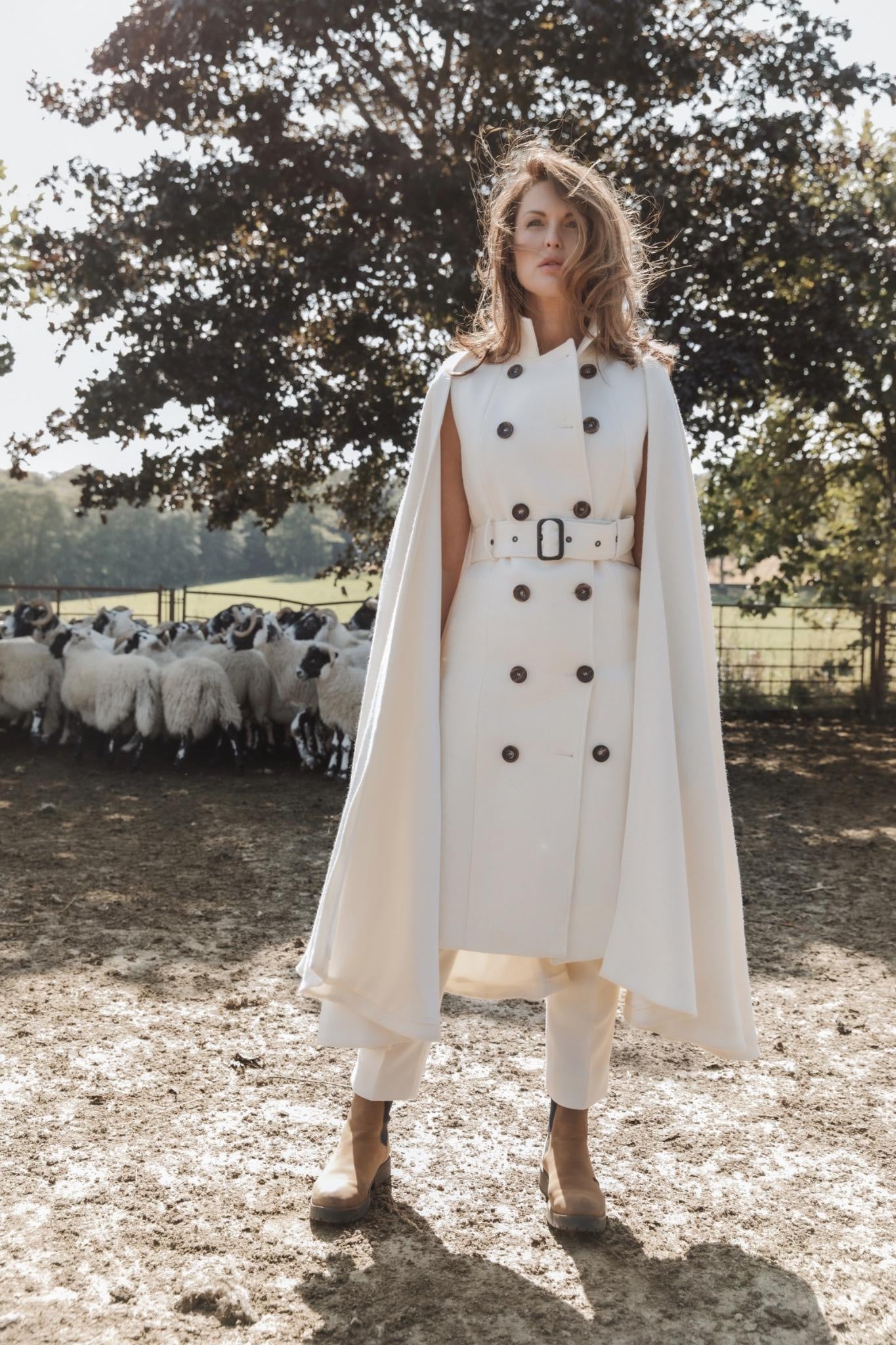 Nadia Alexander stands in a white coat, framed by the flock that began her story, on the very fields of her family farm.